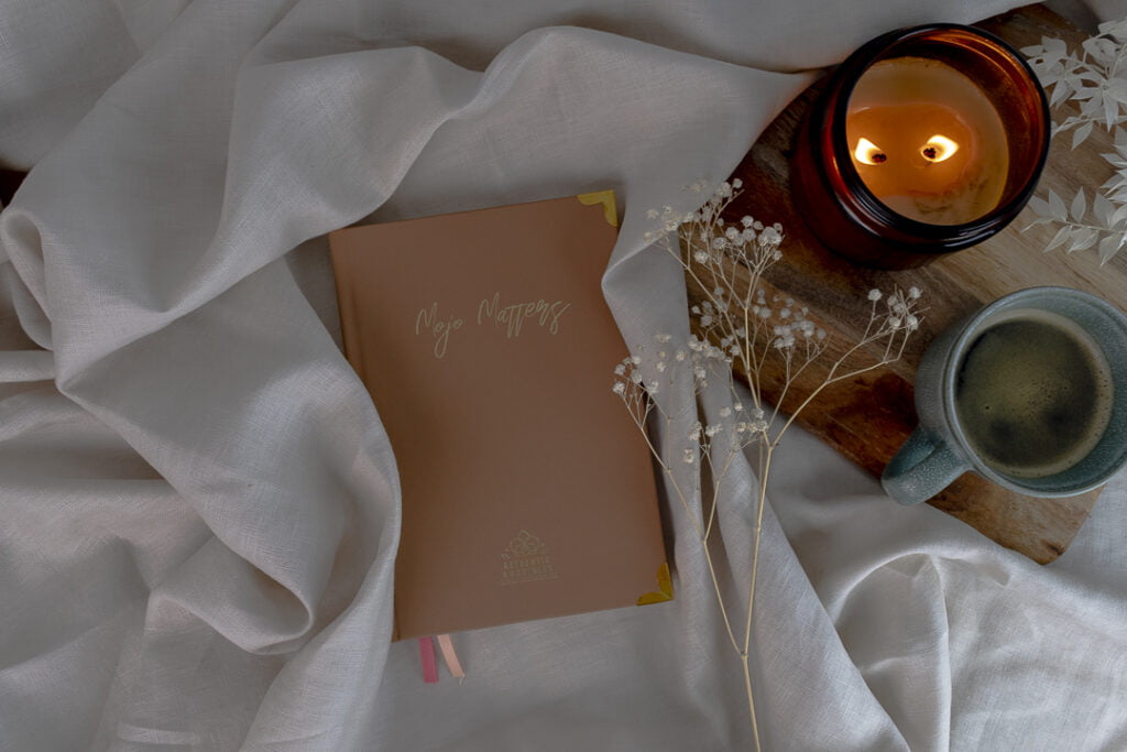 book sitting on a sheet with the words mojo matters on the cover. candle burning and coffee next to book on a wooden board.