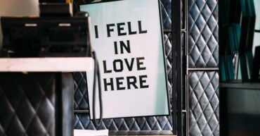 banner saying i fell in love here hanging on a coat hanger in a black room. sign for valentine's day