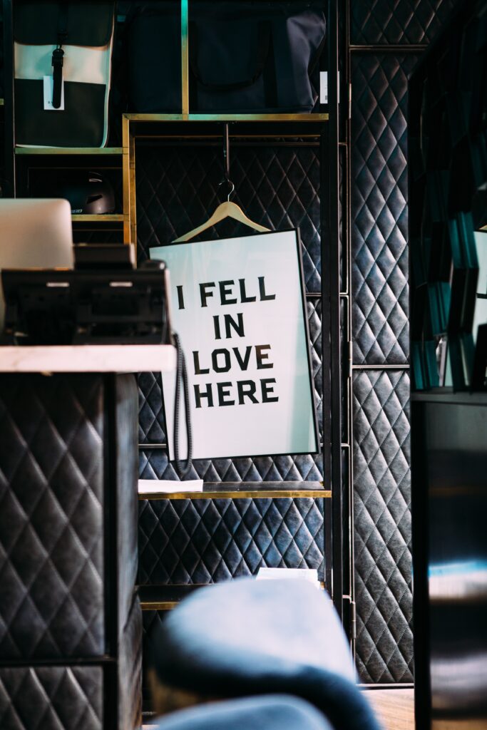 banner saying i fell in love here hanging on a coat hanger in a black room. sign for valentine's day