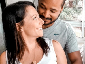 brunette woman sitting in front of black man. woman is looking back at the man. The man is looking down at the woman