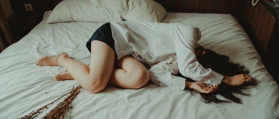 woman lying on her side on bed covering her face wishing for more connection and intimacy after sex