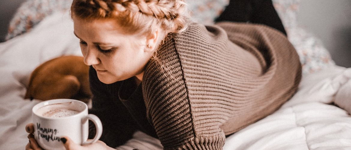 sad woman lying on bed looking into coffee cup thinking about issues with painful sex and how to stop it