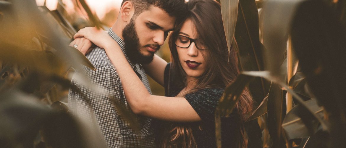 couple looking down contemplating relationship, man and woman hugging amongst foliage