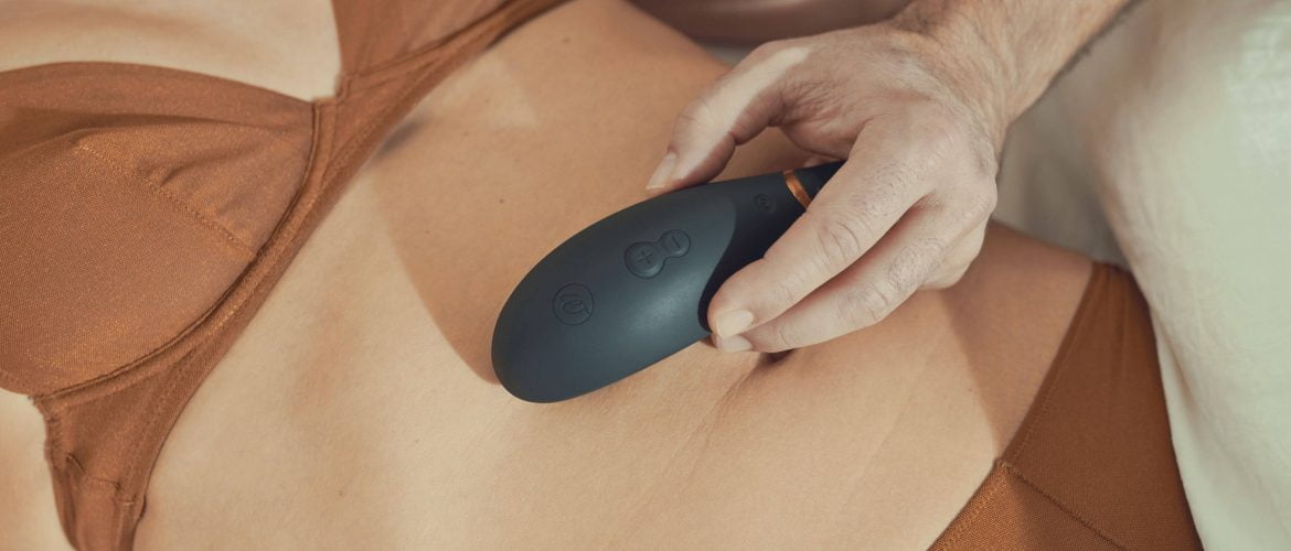 male hand holding a vibrator on a female stomach. Female lying on bed in underwear with vibrator on her stomach. Couple using sex toys to enhance their sexual activities