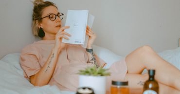 woman lying on bed reading with knee up.