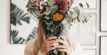 woman holding flowesr up in from of her face, hiding face behind flowers.