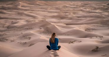 woman sitting on sand dune in a desert. blonde woman sitting with her back to camera