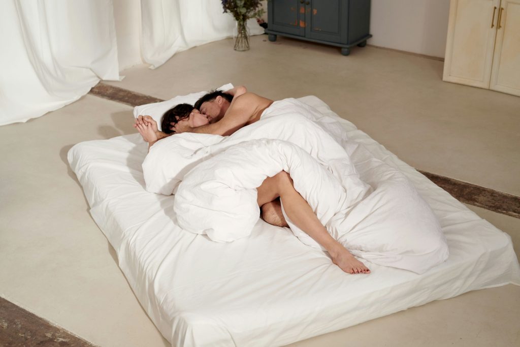 man pleasuring woman. man and woman kissing on a mattress on the floor