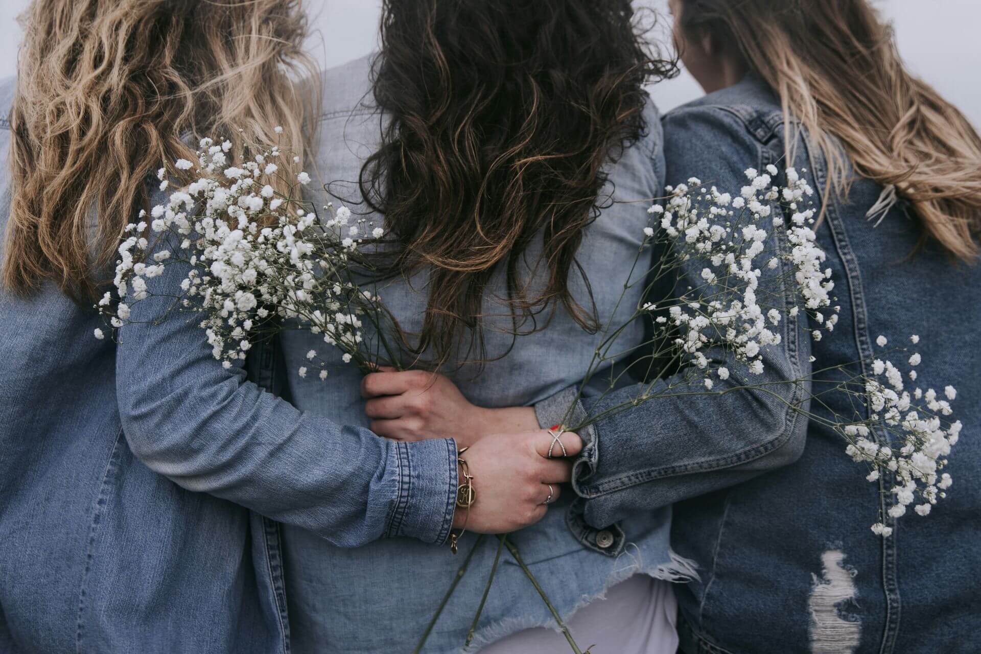 3 women hugging with backs to the camera, holding white flowers