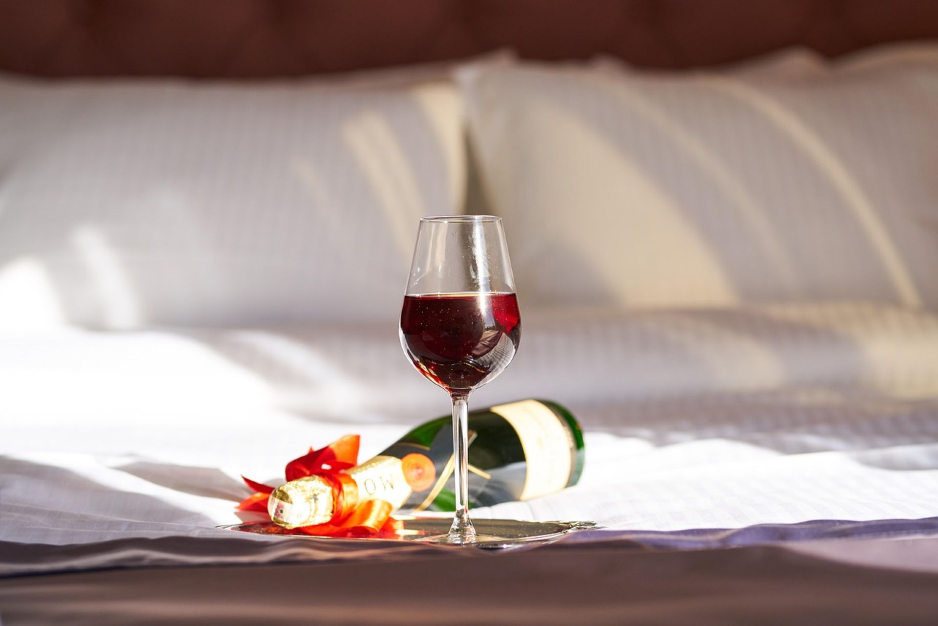 red wine in glass on bed with a champagne bottle lying on the white bed.